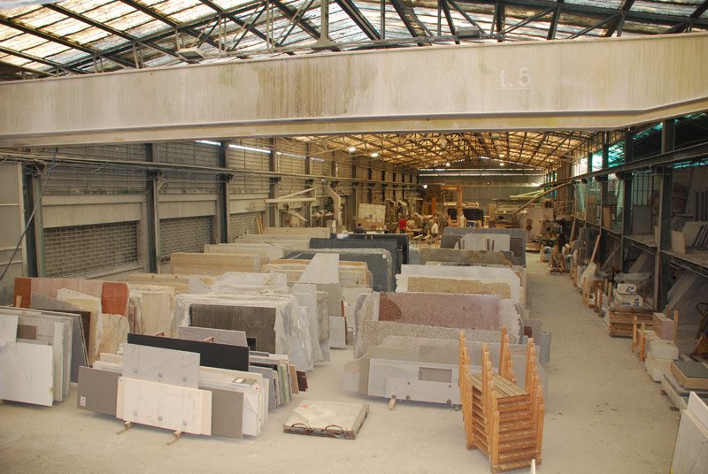 Vue d’ensemble d’un atelier de marbrerie avec stockage de dalles de marbre, quartzite, granit et pierres naturelles destinées à des projets sur mesure.