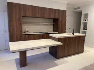 Cuisine moderne avec îlot central, table intégrée et plan de travail en céramique effet travertin beige.