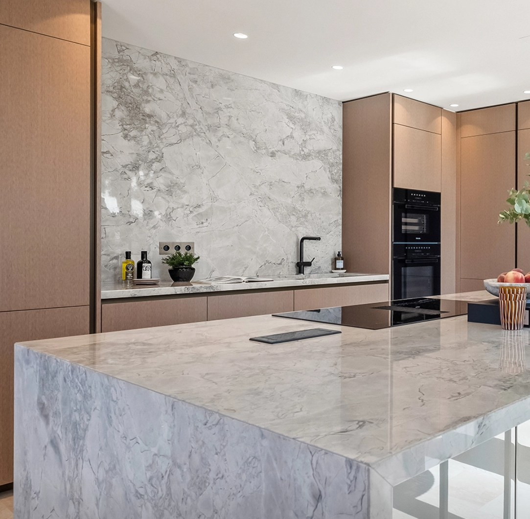 Cuisine contemporaine avec îlot central, plan de travail et crédence en Super White Calacatta, pierre naturelle haut de gamme aux veines grises élégantes.