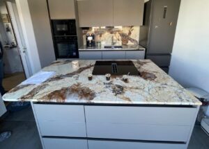 Cuisine contemporaine avec îlot central, plan de travail et crédence en quartzite Patagonia aux veinages bruns, dorés et ivoire.