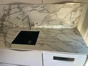 Plan de travail et crédence en céramique Calacatta avec évier sous-plan noir intégré dans une cuisine contemporaine.