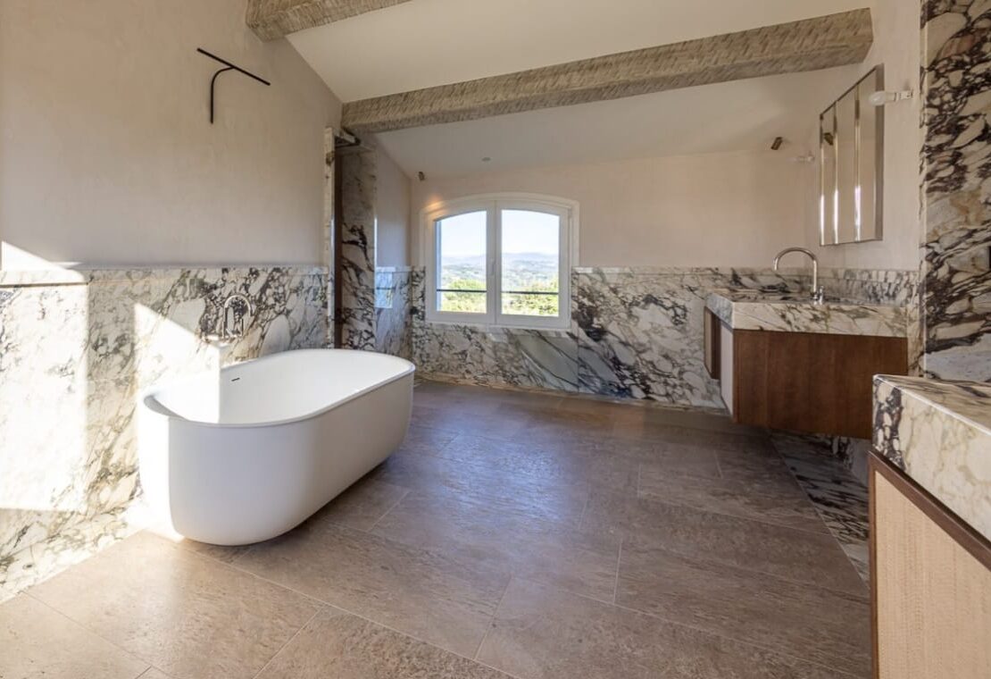 Salle de bain de luxe habillée en marbre Calacatta Viola avec baignoire îlot, vasque suspendue et revêtements muraux en pierre naturelle.