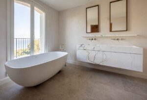 Salle de bains haut de gamme avec meuble suspendu en marbre, double vasque intégrée et baignoire îlot face à une vue panoramique.
