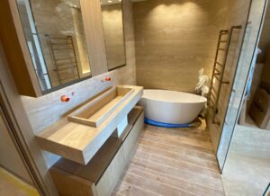 Salle de bains haut de gamme en travertin beige avec vasque monolithique sur mesure, habillages muraux en pierre naturelle et baignoire îlot.